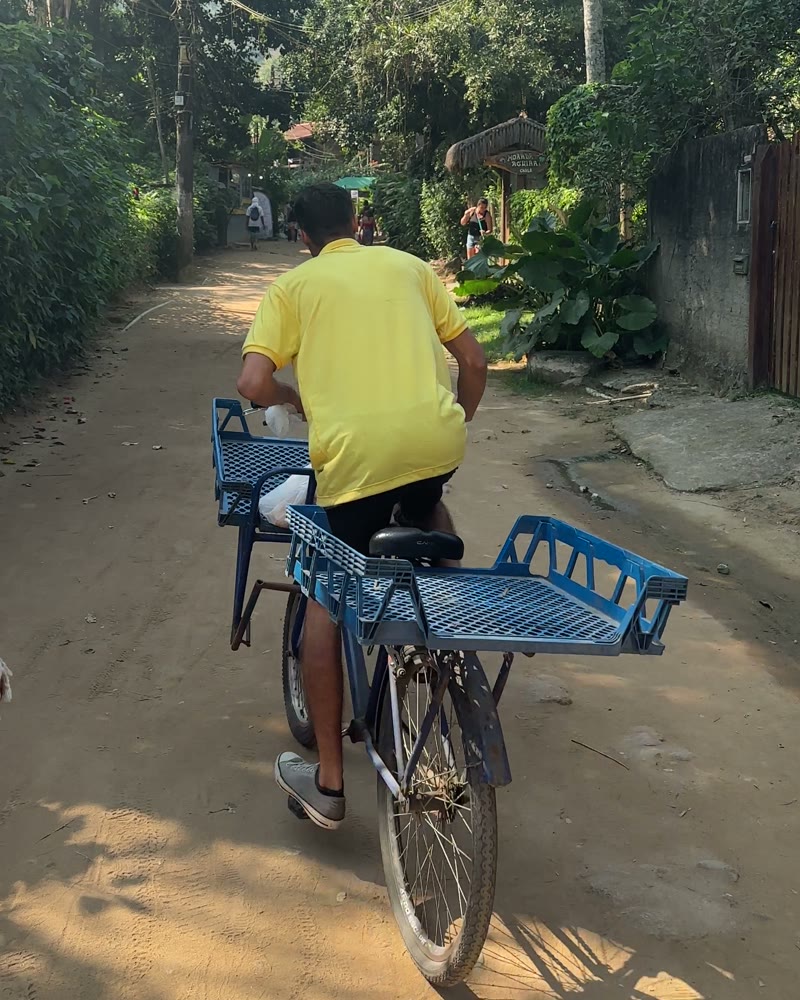 Mann auf einem Fahrrad mit Transportkiste auf einem Sandweg in Abraão