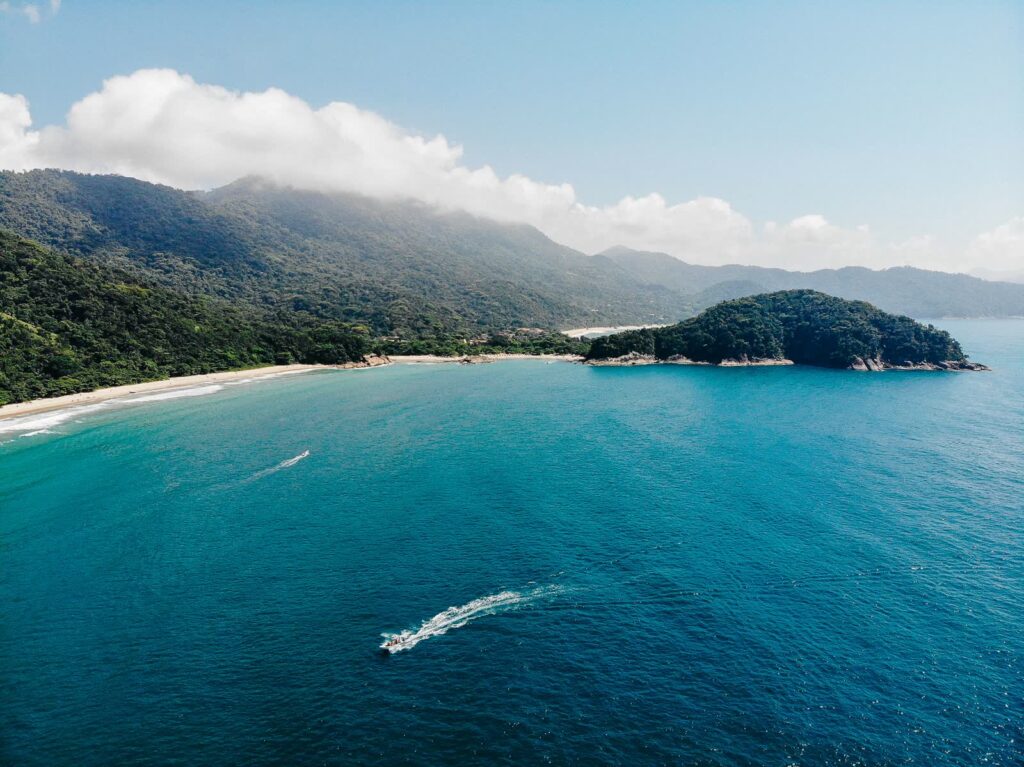 Küste der Ilha Grande aus der Luft mit bewaldeten Hängen, Sandstrand und Schnellboot, Bundesstaat Rio de Janeiro