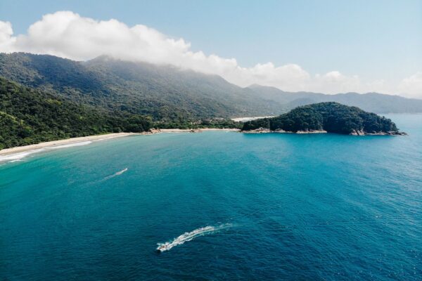 Küste der Ilha Grande aus der Luft mit bewaldeten Hängen, Sandstrand und Schnellboot, Bundesstaat Rio de Janeiro